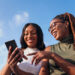 two young African women having fun together while looking at a smartphone